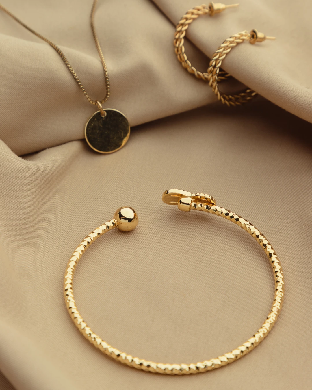 Gold bracelet, necklace and hoop earrings on soft beige fabric