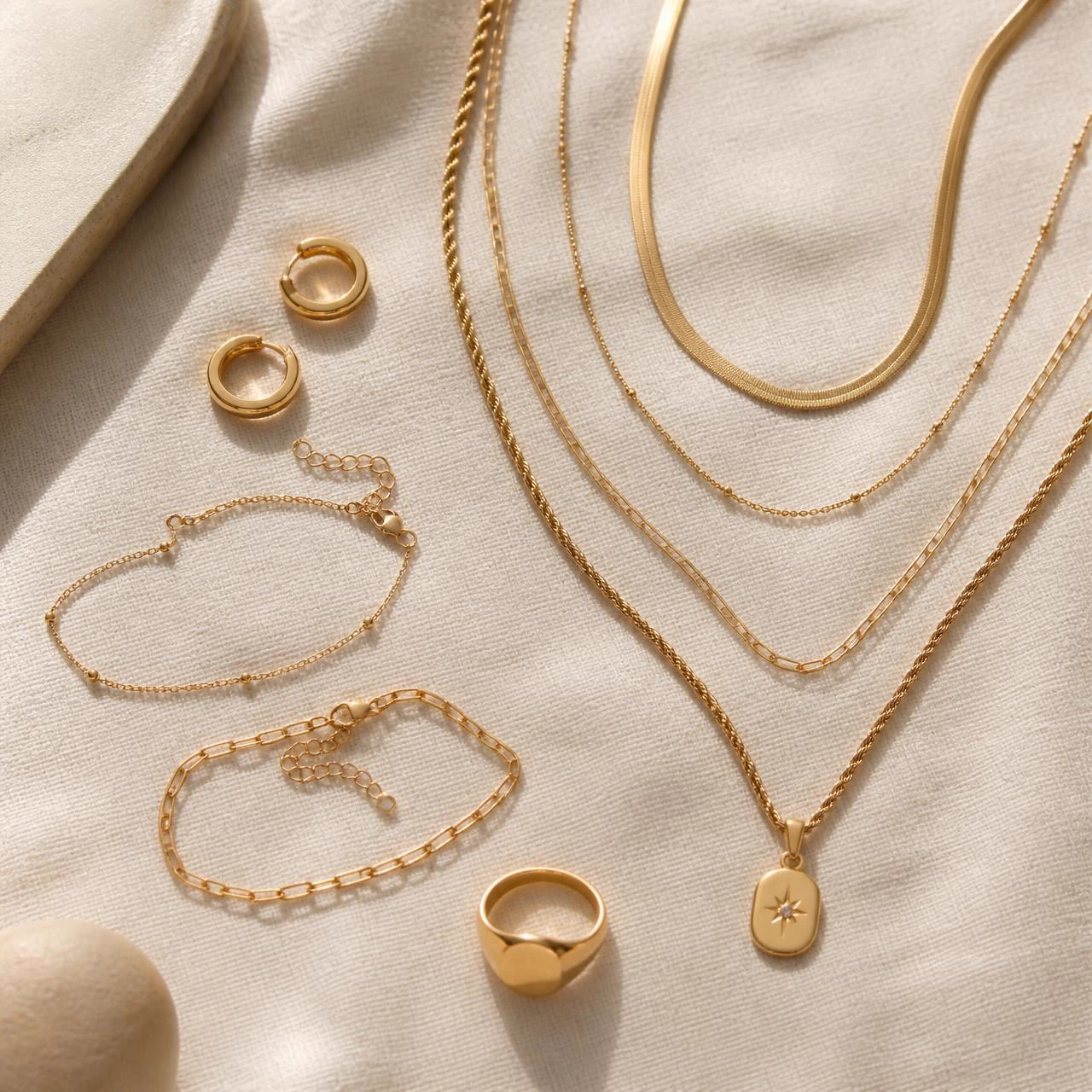 Flat lay of 18k gold filled chains, bracelets, hoops and signet ring on cream linen